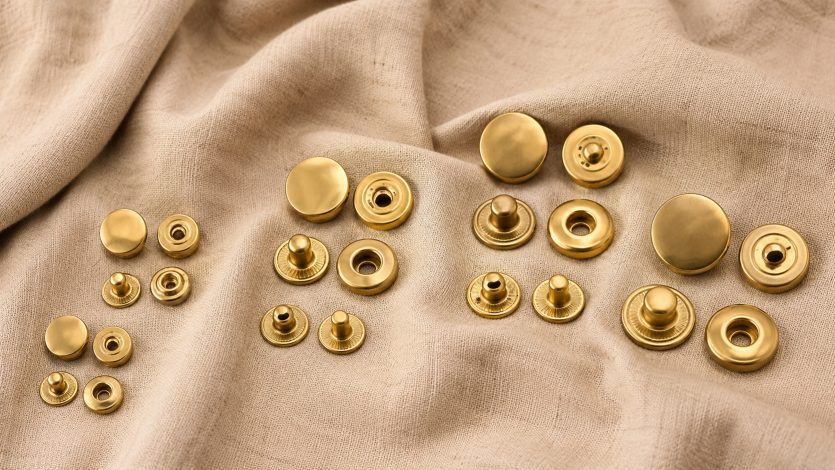 golden snaps, Golden snaps in multiple sizes are displayed with matching metal components on beige fabric.